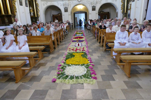 Dywan kwiatowy porodku kocioa. Po lewej i po prawej stronie s ludzie siedzcy w awkach.