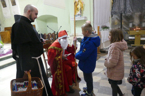 w. Mikoaj rozdajcy dzieciom prezenty w kociele. Po jego prawej stronie stoi franciszkanin z koszykiem. 