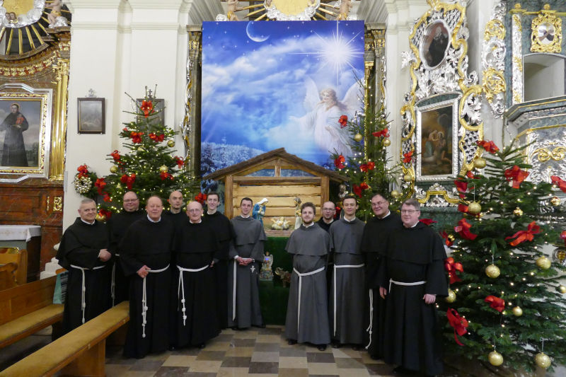 Ojcowie i Bracia Franciszkanie stojcy przy szopce.