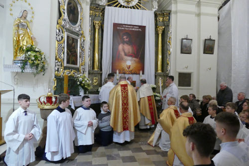 Kapłani ubrani w złote szaty składają Ciało Pana Jezusa w Ciemnicy. Wokół nich klęczą ministranci.