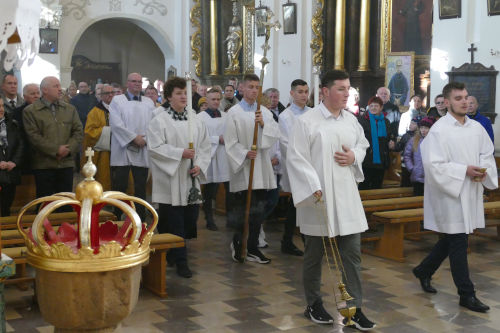 Ministranci wchodzcy do kocioa z kadzidem i Krzyem. Po lewej stronie na pierwszym planie chrzcielnica. W tle w awkach stoj wierni.